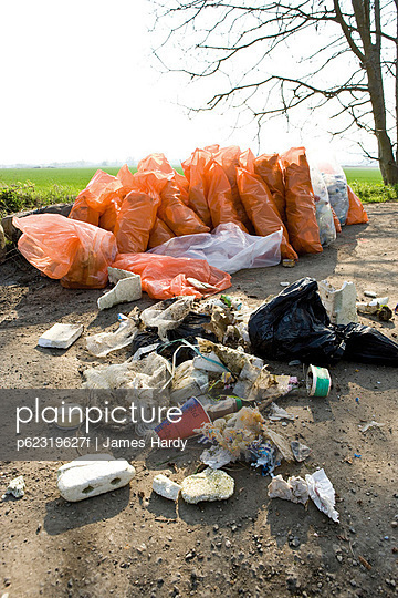 Trash dumped outdoors; full bags of trash in background result of cleanup effort