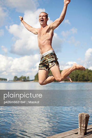 Excited mature man jumping into lake