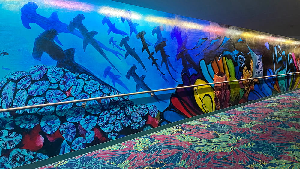 Painting of jammerhead sharks swimming over a colorful reef of coral and sponges in a section of the Aquarius Art Tunnel