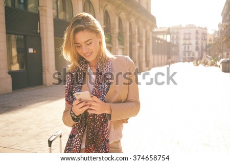 gorgeous beautiful young woman with blonde hair messaging on the smart-phone at the city street background. pretty girl having smart phone conversation in sun flare.