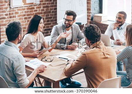 Making great decisions. Young beautiful woman gesturing and discussing something with smile while her coworkers listening to her sitting at the office table