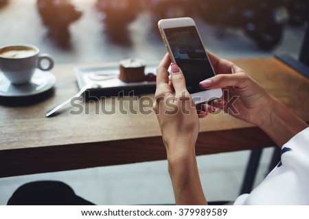 Close up of women\'s hands holding cell telephone with blank copy space scree for your advertising text message or promotional content, hipster girl watching video on mobile phone during coffee break