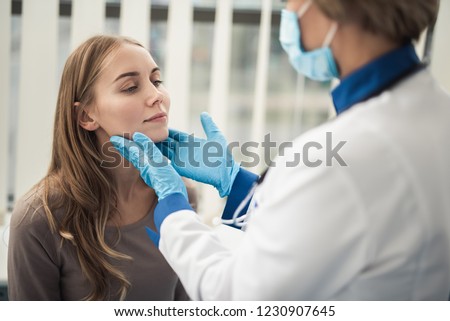 Concept of professional consultation in therapist system. Close up portrait of doctor woman examining tonsils of smiling young lady in medical office