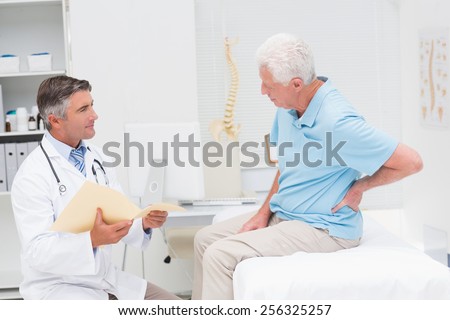 Male doctor discussing reports with senior patient suffering from back pain in clinic