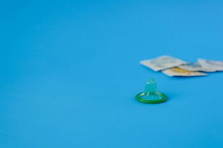 Green condom on blue paper background with copy space for text. Reproductive health, contraception and safe sex concept