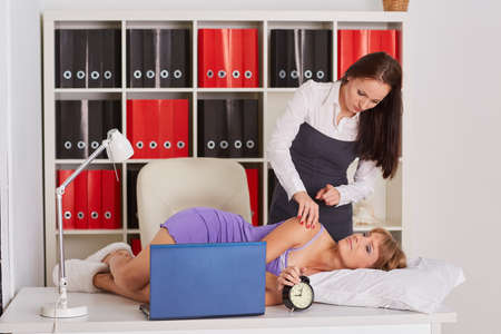 Young business woman tries to wake the sleeping coworker on a workplace in the office. Overworked.