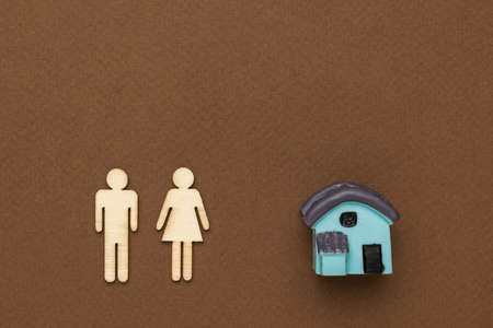 Male and female wooden silhouettes and a model of a house on a brown background. The concept of a family home. Flat lay.