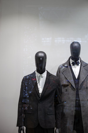 two black male mannequins in dark suits and coats on a shop window with bokeh from festive lights.