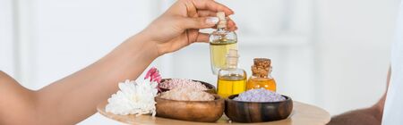 panoramic shot of woman taking bottle with oil while masseur holding tray