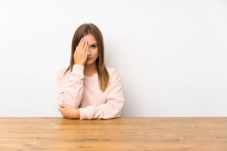 Teenager girl in a table covering a eye by hand