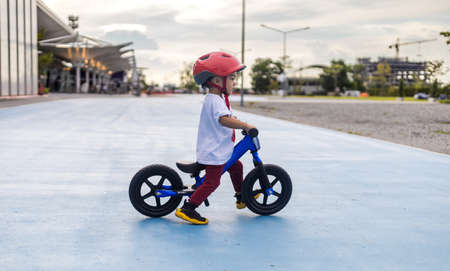 Adorable Asian kid boy (Toddler age 1-year-old), Wearing a Safety Helmet and Learning to Ride a Balance Bike in the Play Space. Baby Playground and Safe Place Concept. Portrait Photo with Copy Space.