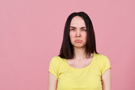 upset by the caricature of a sad brunette girl in yellow shirt, makes a face and sticks out lower lip. Large Studio portrait on a pink background, negative emotions, failure, bad news, disappointment