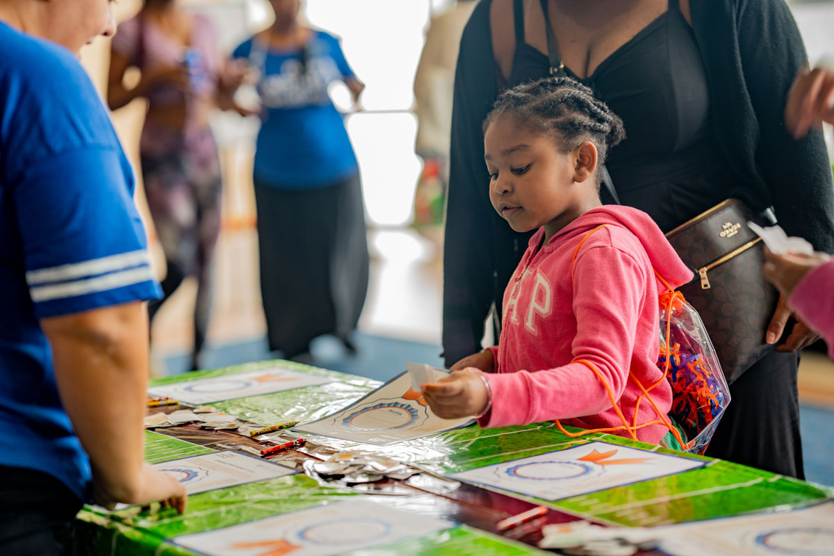 A young girl in a pink jacket stands in front of a table at a reading event