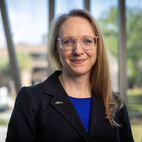 A female faculty member standing outside wearing a royal blue blouse and black jacket.