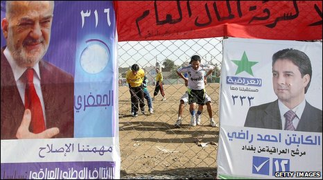 Iraqi youths play football in a field adorned with campaign posters