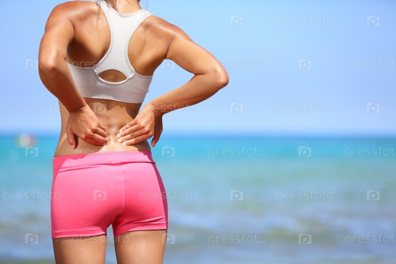 Back Pain. Athletic Woman In Pink Sportswear Standing At The Seaside Rubbing The Muscles Of Her Lower Back, Cropped Torso Portrait.