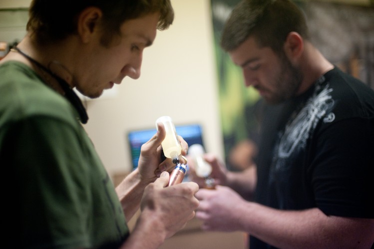 Elijah Seybold, left, fills his e-cigarette device alongside Nathan Waller. Before contests, some competitors tune up their devices, twisting resistant wire into coils to carry electricity from their vaporizer’s battery, and weaving dry cotton through the coils.