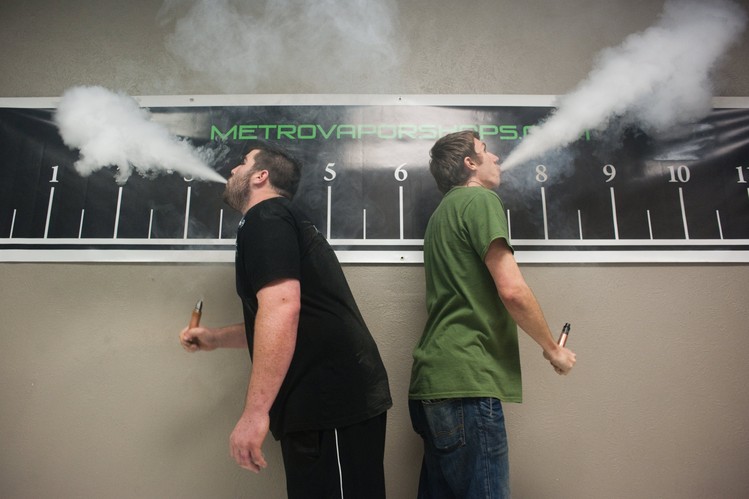 Nathan Waller, left, competes alongside Elijah Seybold, right, in their face-off in the Clouds for Heroes vape competition at Metro Vapors in Plano, Texas. Contestants using e-cigarette devices vie to create the biggest vapor cloud.