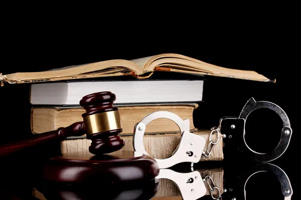 Gavel, handcuffs and books on law isolated on black close-up