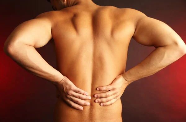 Young man with back pain on dark background