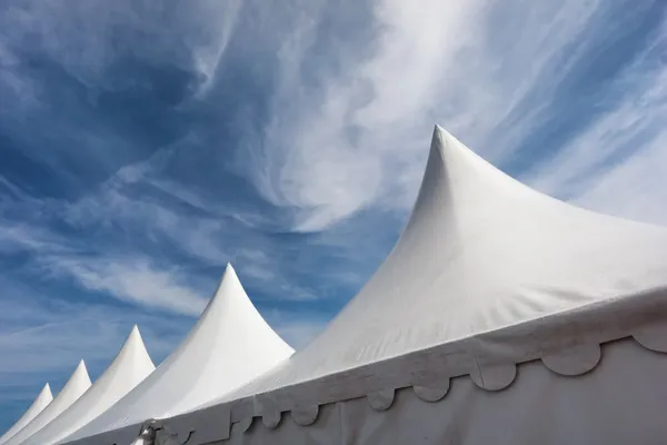 Row of white event and party tents against blue sky