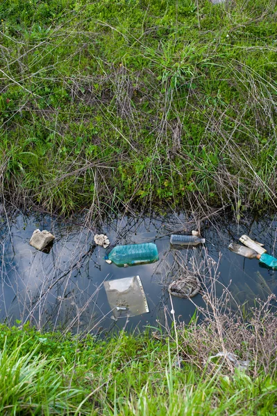 Concept or conceptual unhygienic polluted river,sewage or dirty water and grass with waste,trash and dump background