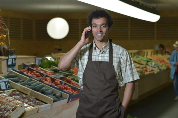 Grocery clerk phoning in produce aisle of supermarket store