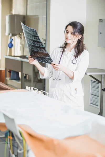 Beautiful girl doctor in a white coat examines X-ray photo of the patient to identify the problem. Professional conversation, consultation of doctors. The work of the conference.