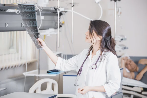 Beautiful girl doctor in a white coat examines X-ray photo of the patient to identify the problem. Professional conversation, consultation of doctors. The work of the conference