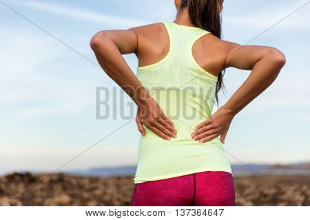 Trail running runner with painful lower back pain injury or strained muscle near the spine. Female a