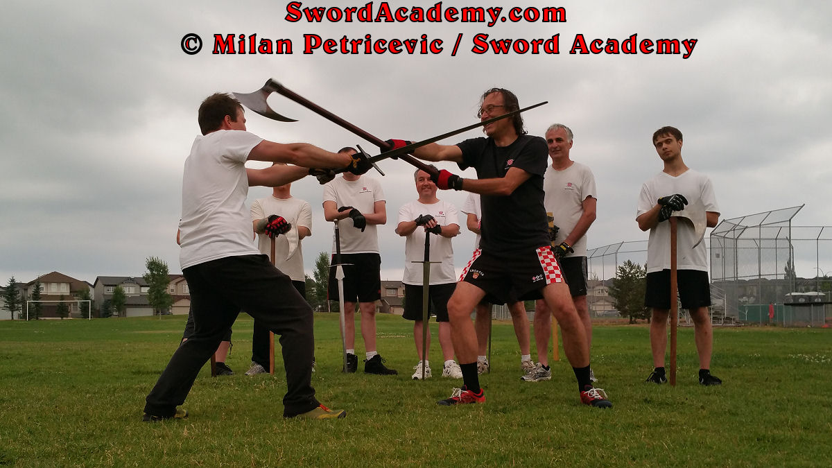 Milan demonstrates during an outdoor class in front of Sword Academy students two handed axe attack against the longsword exercise attacking from both sides as inspired by historical sources from the German medieval (and renaissance) tradition, part of Sword Academy HEMA / WMA / Martial Arts curriculum.