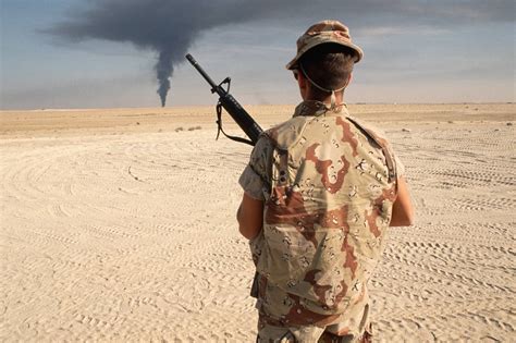 A US soldier stands in the desert as a Kuwaiti oil rig burns out of ...