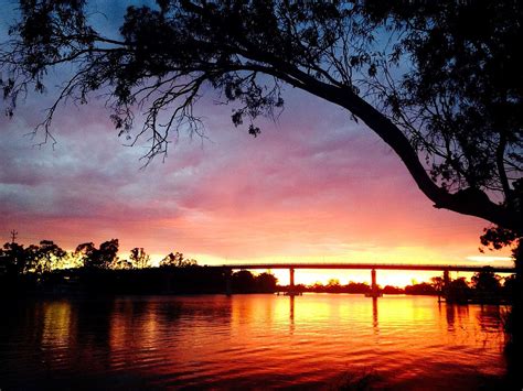 the sun is setting behind a bridge over a body of water with trees in ...