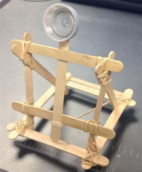 A photograph shows a small catapult structure made from Popsicle sticks ...