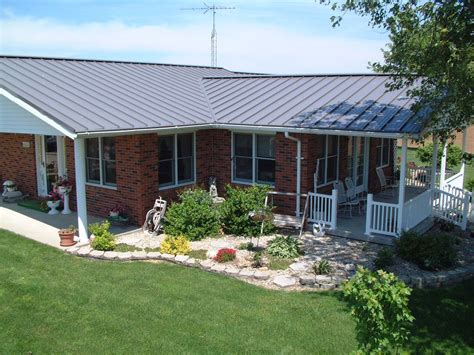 a brick house with a metal roof and white porch railings on the front lawn