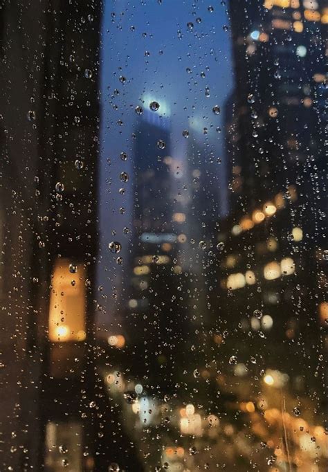 rain drops on the window and buildings in the background at night, with ...