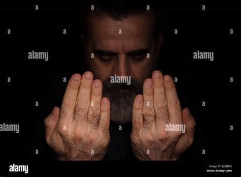 Man raising hands in prayer, in a dark room and with black background ...