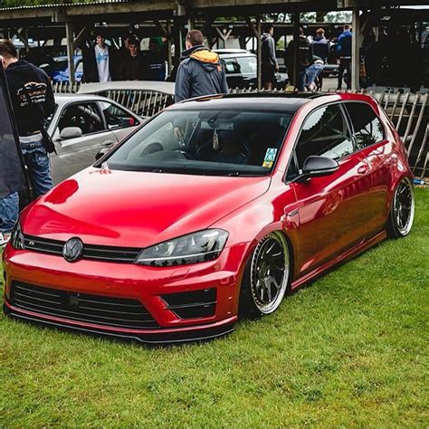 a red car parked on top of a lush green field next to other cars and people