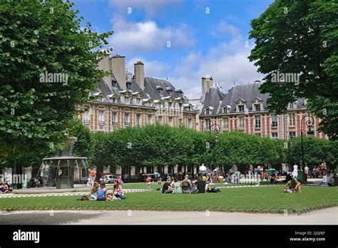 Families with children relax on the lawn of the Place des Vosges ...