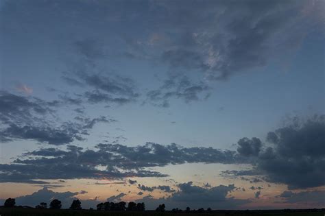 the sky is blue and cloudy at dusk with clouds in the foreground, trees ...