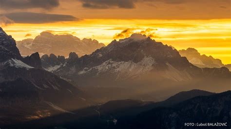 the mountains are covered in snow as the sun sets over them and light ...