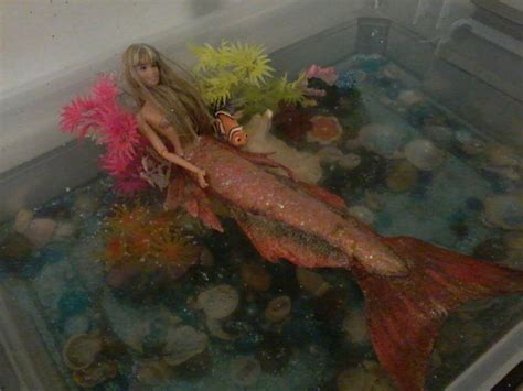 a barbie doll is sitting on the bottom of a fish tank