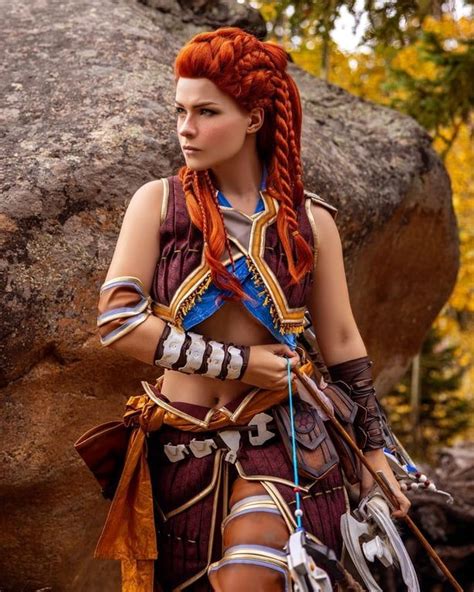 a woman with red hair and braids standing in front of a rock wearing armor