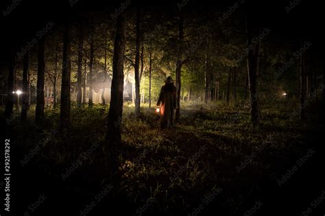 strange light in a dark forest at night. Silhouette of person standing ...