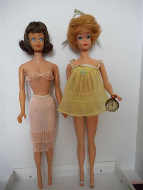 two dolls standing next to each other in front of a wall with a clock on it