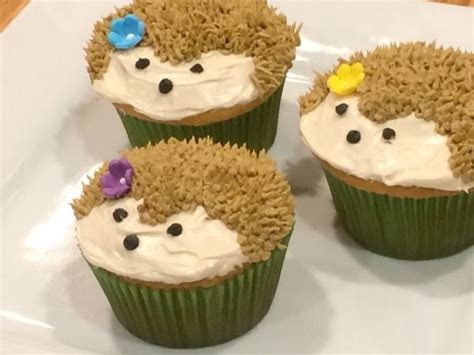 three cupcakes with white frosting and hedgehog faces on them sitting ...