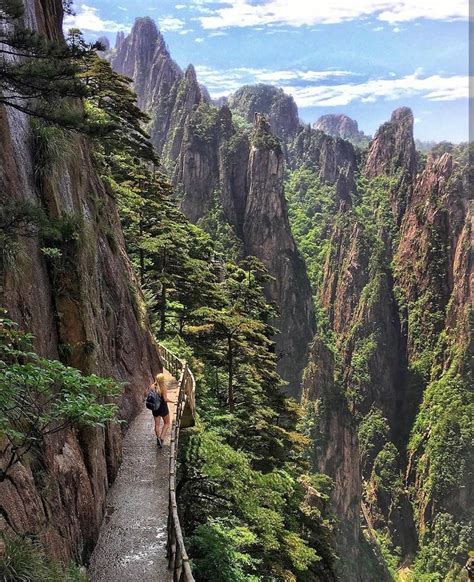 two people walking down a path in the mountains with trees on both ...