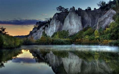 the sun is setting over some mountains and trees on the water's edge ...