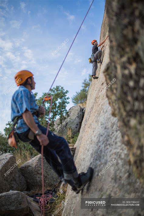 Adventurers climbing mountain, wearing safety harness against ...