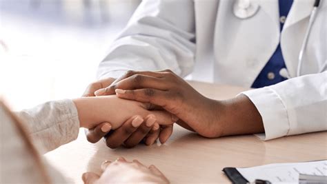 A doctor's hands hold a patient's from across a table.